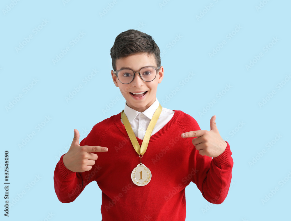 Smart little school boy with golden medal on light blue background