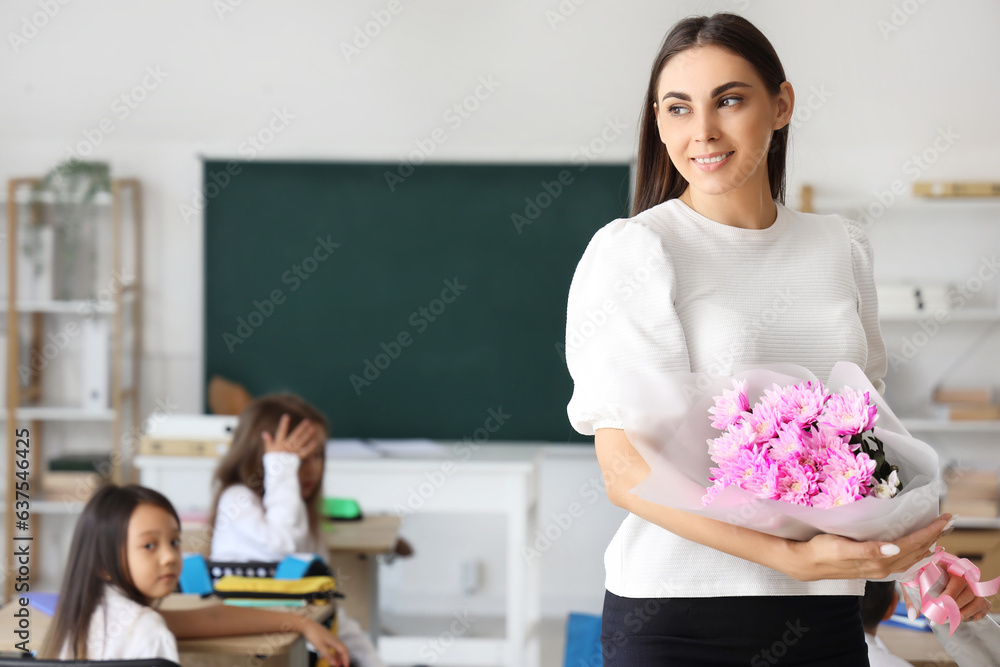 Young female teacher with bouquet of flowers in classroom