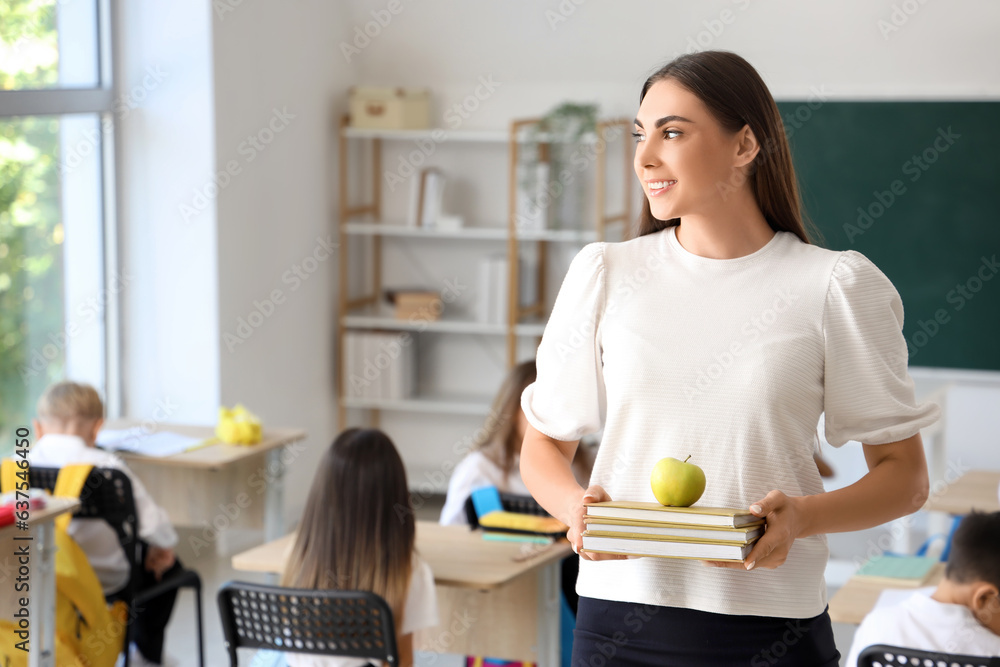 Young female teacher with books and apple in classroom