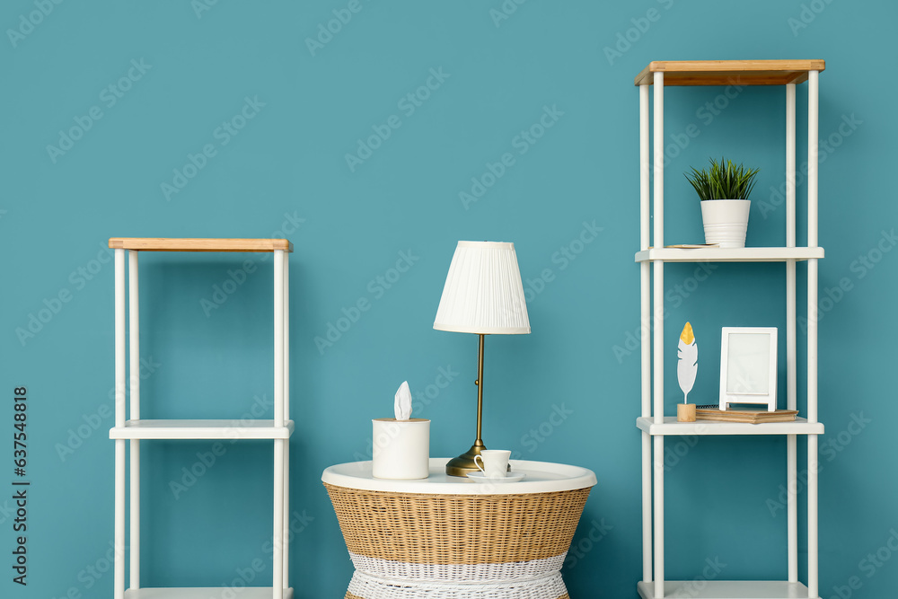 Lamp on small table and shelving units near blue wall