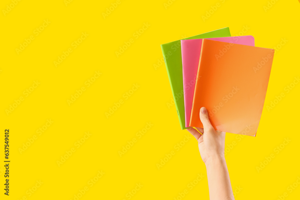 Hand with notebooks on yellow background