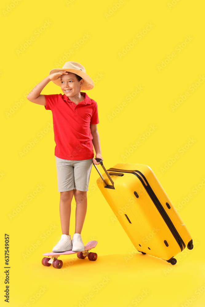 Little African-American boy with suitcase and skateboard on yellow background