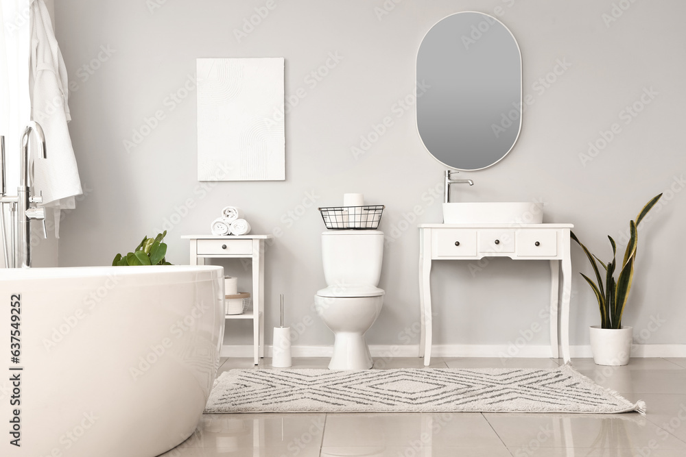 Interior of light restroom with ceramic toilet bowl, bathtub and vanities