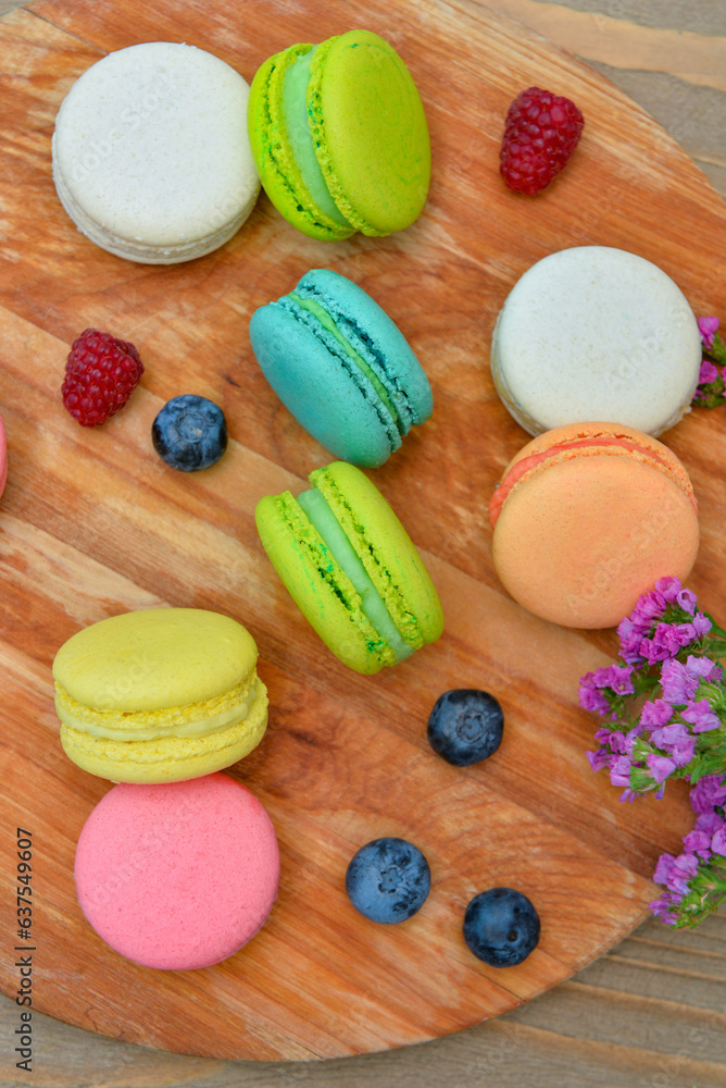 Board with sweet macaroons and berries on wooden background