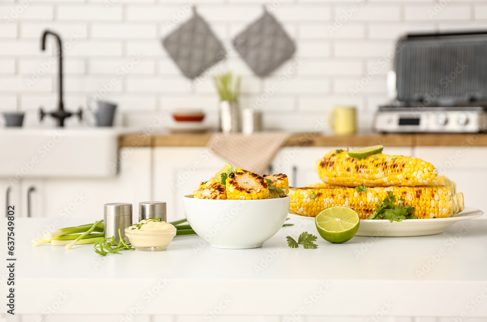 Plate and bowl with tasty grilled corn on table in kitchen