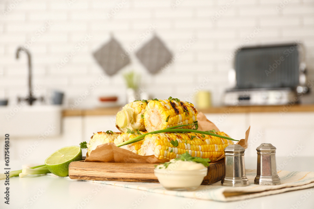 Wooden board with tasty grilled corn on table in kitchen