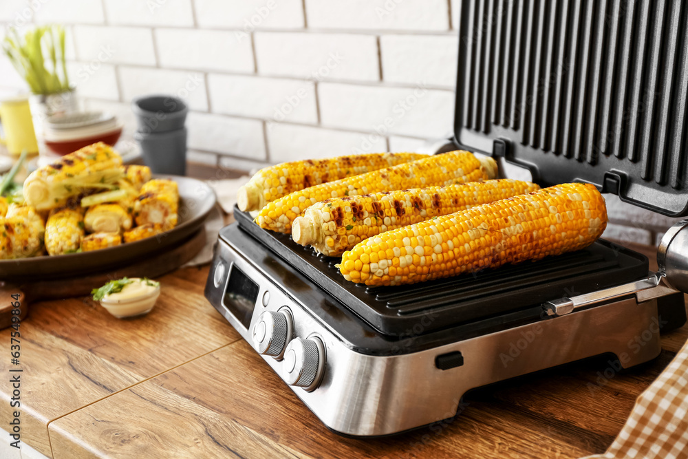 Electric grill with tasty corn on wooden kitchen counter