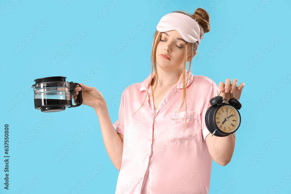 Sleepy young woman with alarm clock and coffee pot on blue background