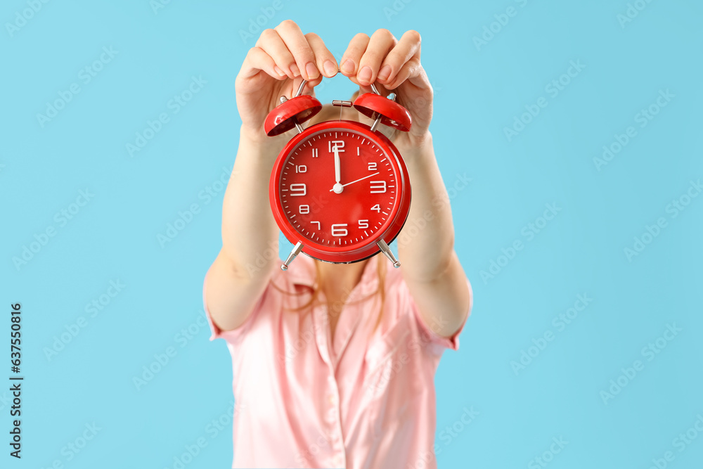 Woman in pajamas with alarm clock on blue background