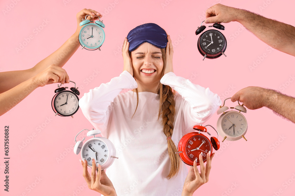 Young woman surrounded by loud alarm clock on pink background