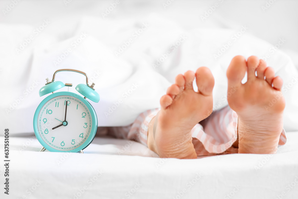 Sleeping womans feet with alarm clock in bed, closeup