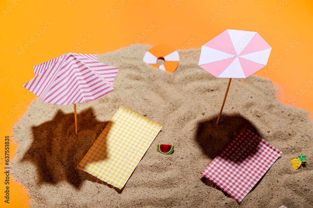 Creative summer composition with mini umbrellas, beach accessories and sand on orange background