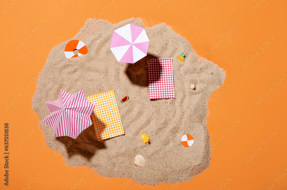 Creative summer composition with mini umbrellas, beach accessories and sand on orange background