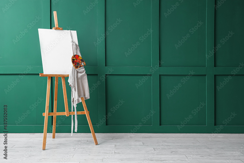 Wooden easel with blank canvas near green wall