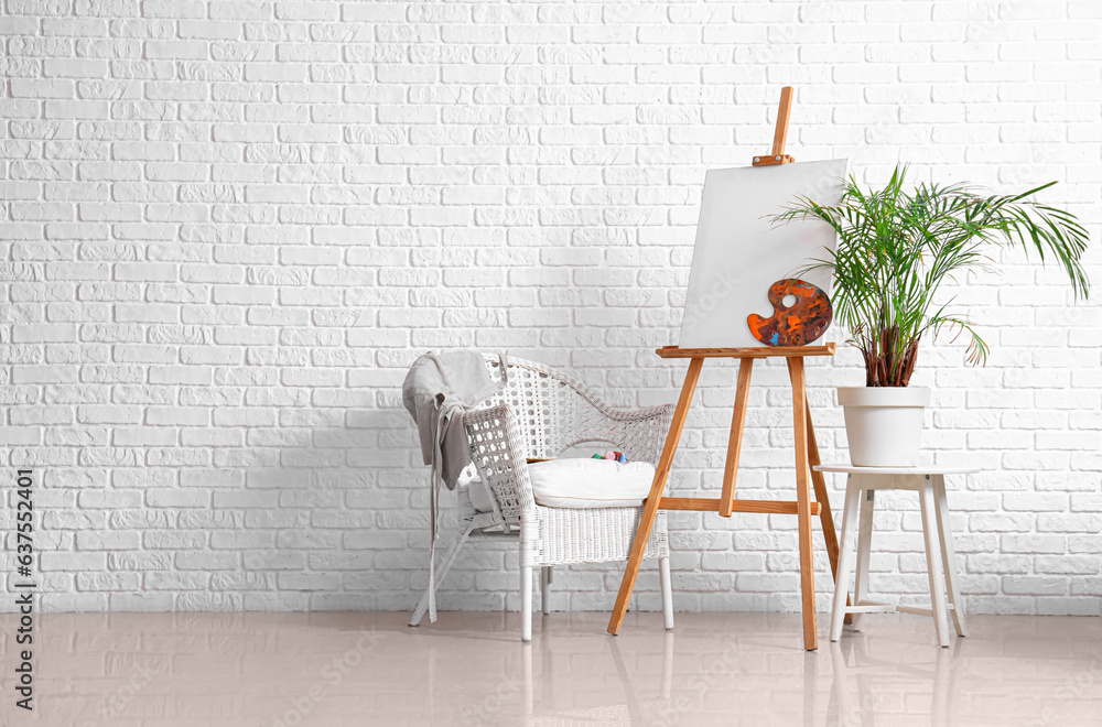 Wooden easel with blank canvas near white brick wall