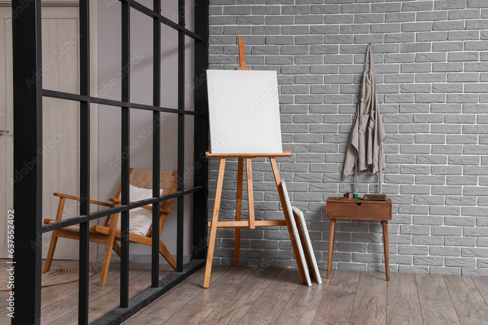 Wooden easel with blank canvas near grey brick wall