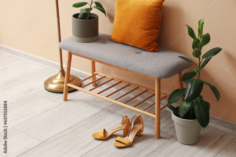 Interior of stylish room with soft bench and female shoes near beige wall