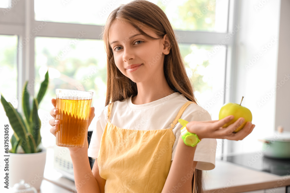 Little girl with glass of juice and apple in kitchen