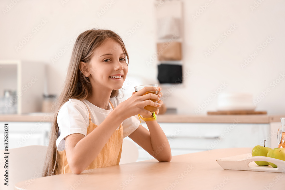 Little girl with glass of apple juice in kitchen