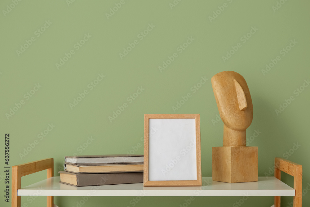 Blank frame with books and decor on shelf near green wall, closeup