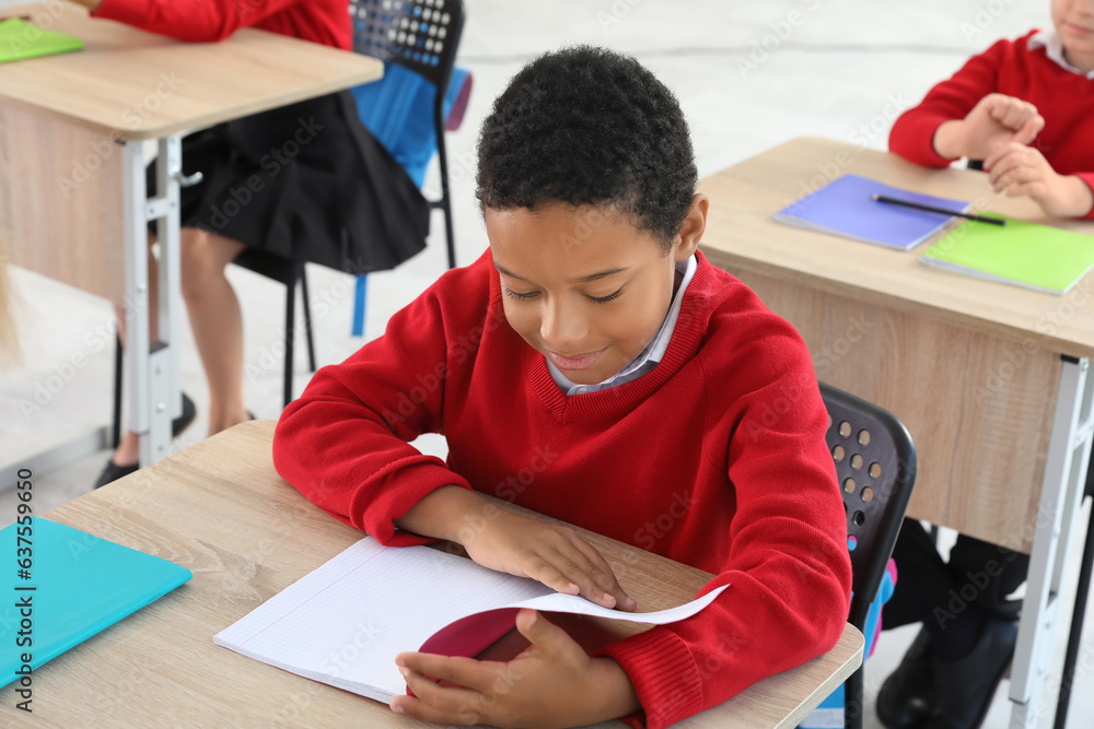 Little African-American schoolboy sitting at desk during lesson in classroom