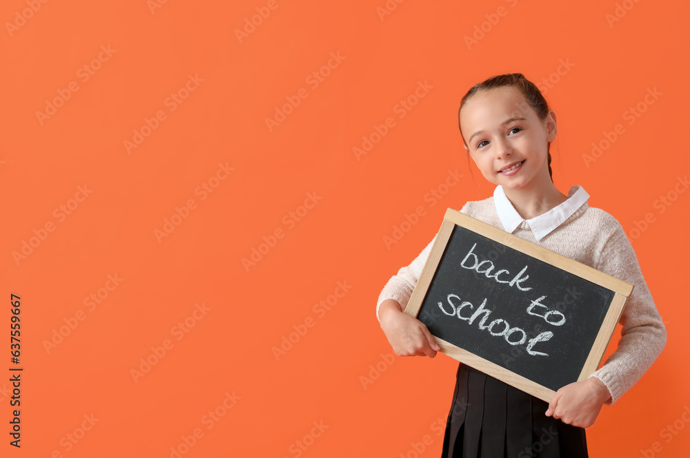 Little schoolgirl in stylish uniform holding blackboard with text BACK TO SCHOOL on orange backgroun