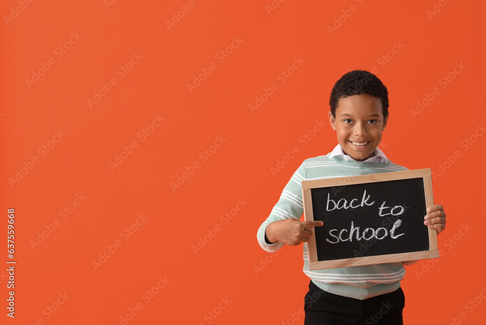 Little African-American schoolboy in stylish uniform holding blackboard with text BACK TO SCHOOL on 