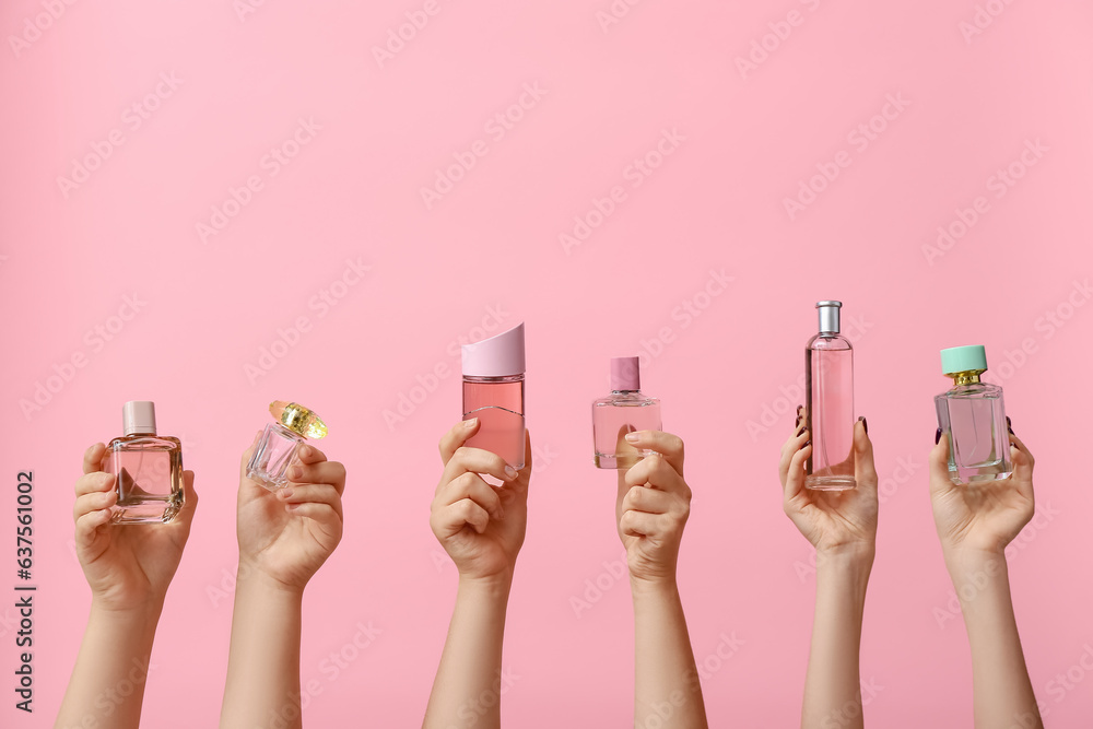 Female hands holding different perfumes on pink background