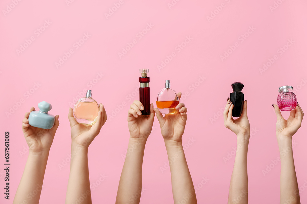 Female hands holding different perfumes on pink background