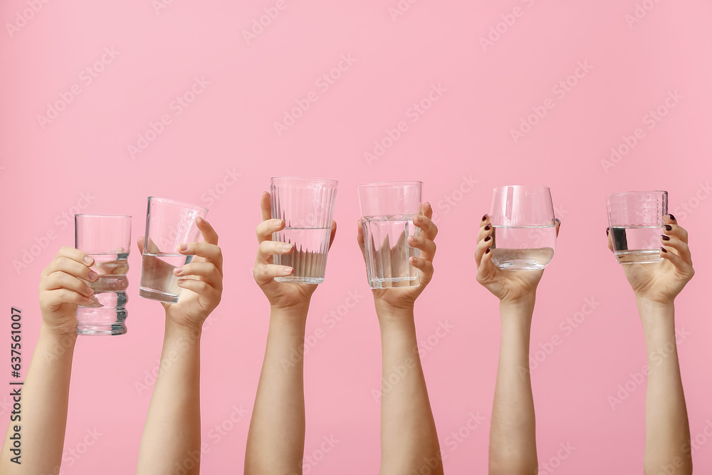 Female hands holding glasses of water on pink background