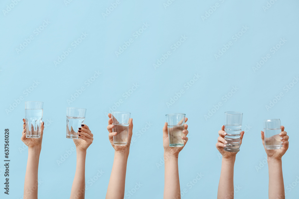 Female hands holding glasses of water on blue background