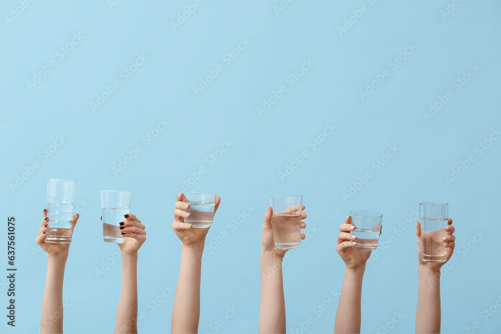 Female hands holding glasses of water on blue background