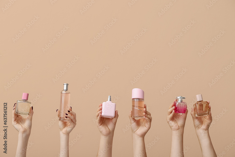 Female hands holding different perfumes on beige background