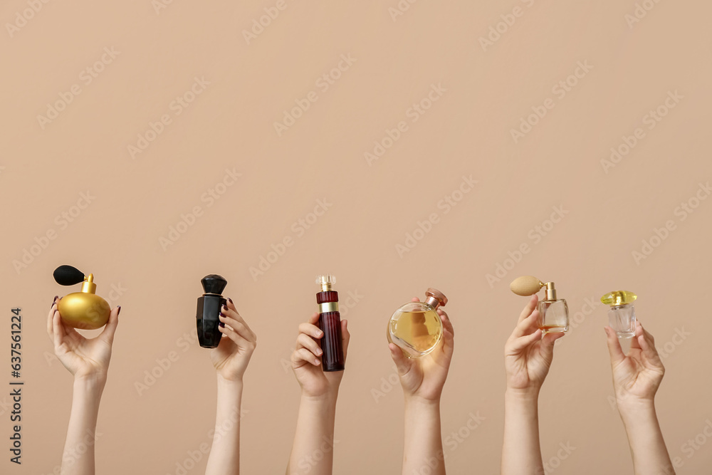 Female hands holding different perfumes on beige background