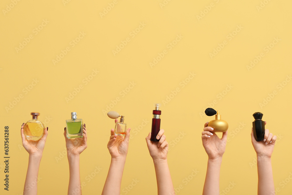 Female hands holding different perfumes on yellow background