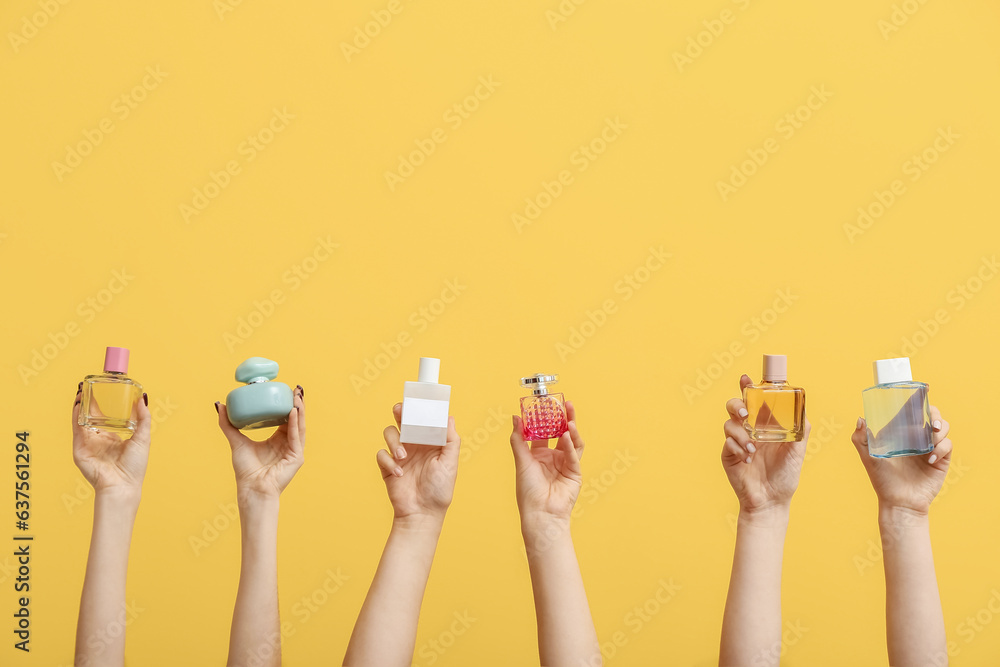 Female hands holding different perfumes on yellow background