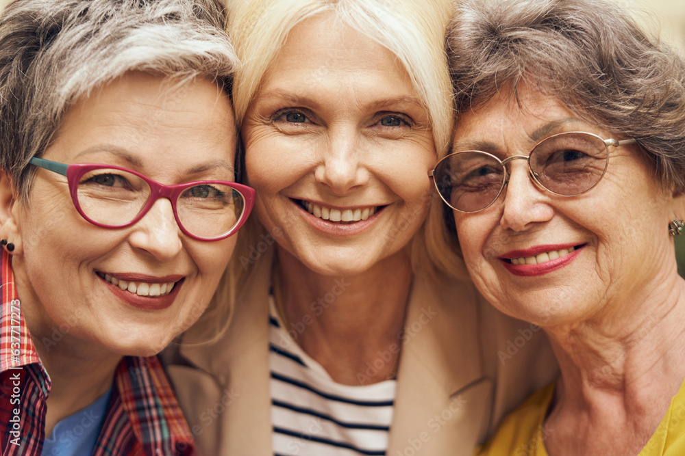 Portrait of happy middle age women hug and look at camera on city street. Female friendship