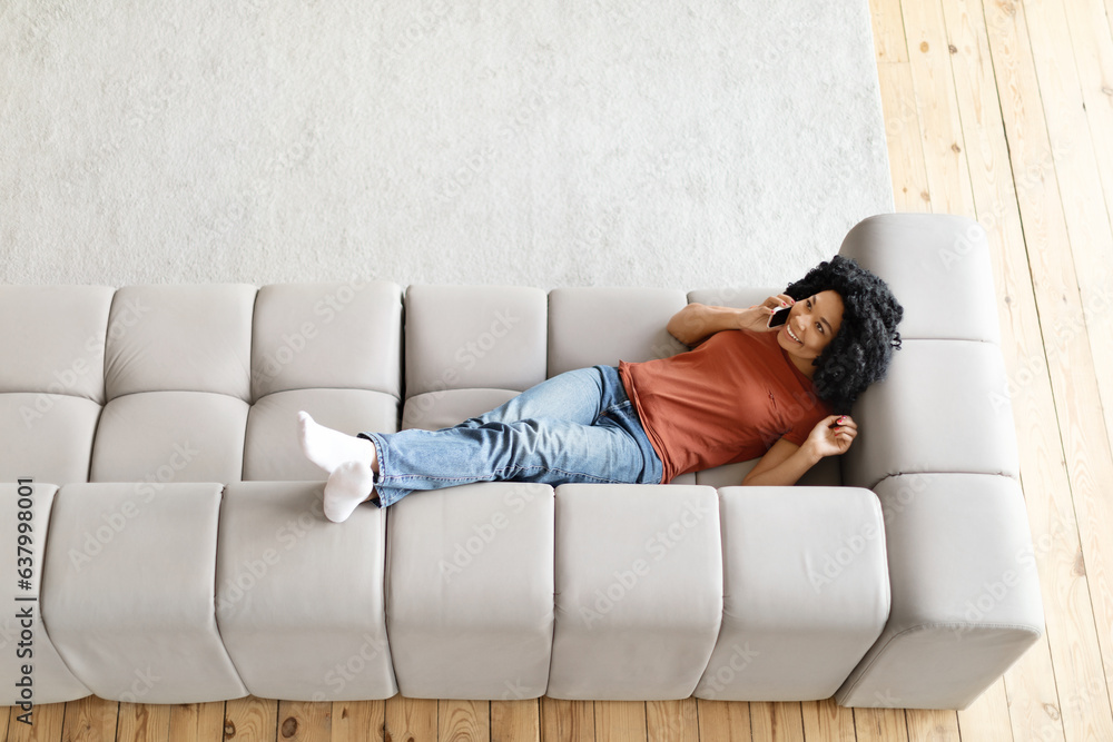 Happy Black Woman Talking On Cellphone While Lying On Couch At Home