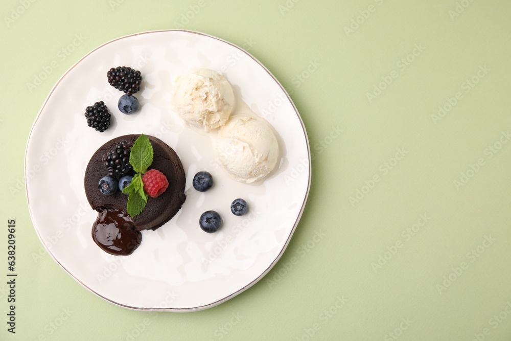 Plate with delicious chocolate fondant, berries, mint and ice cream on light green table, top view. 