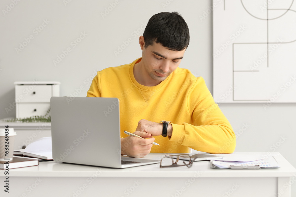 Young man looking at watch while sitting at workplace