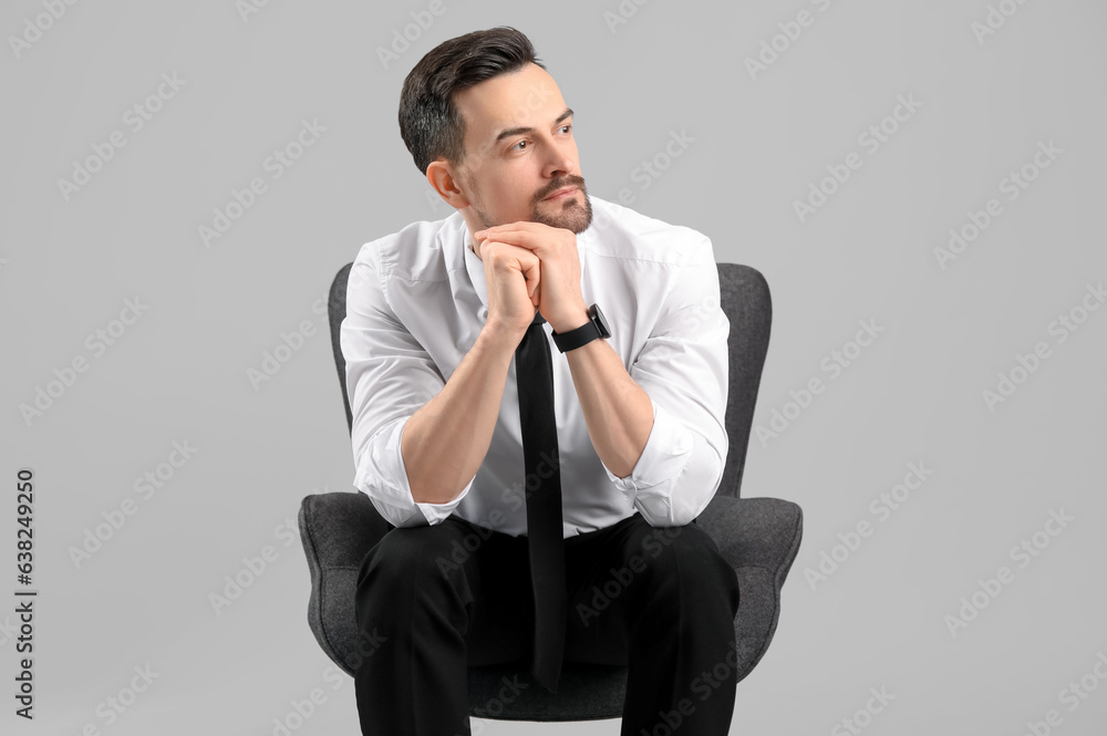 Handsome businessman sitting in armchair on grey background