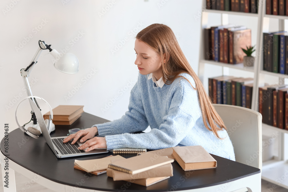 Female student studying with laptop at table in library