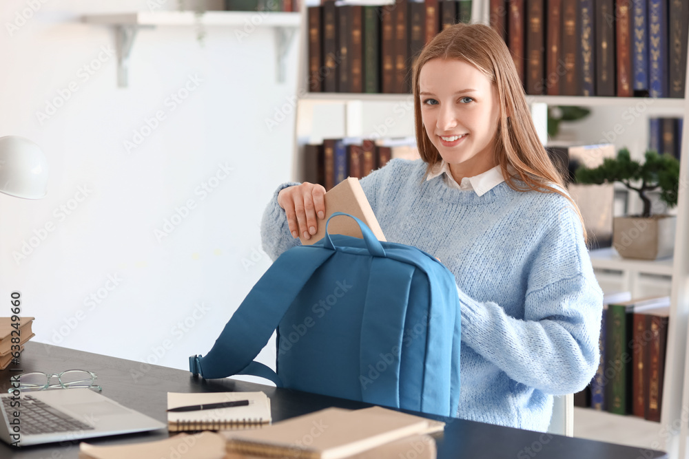 Female student putting book into backpack in library