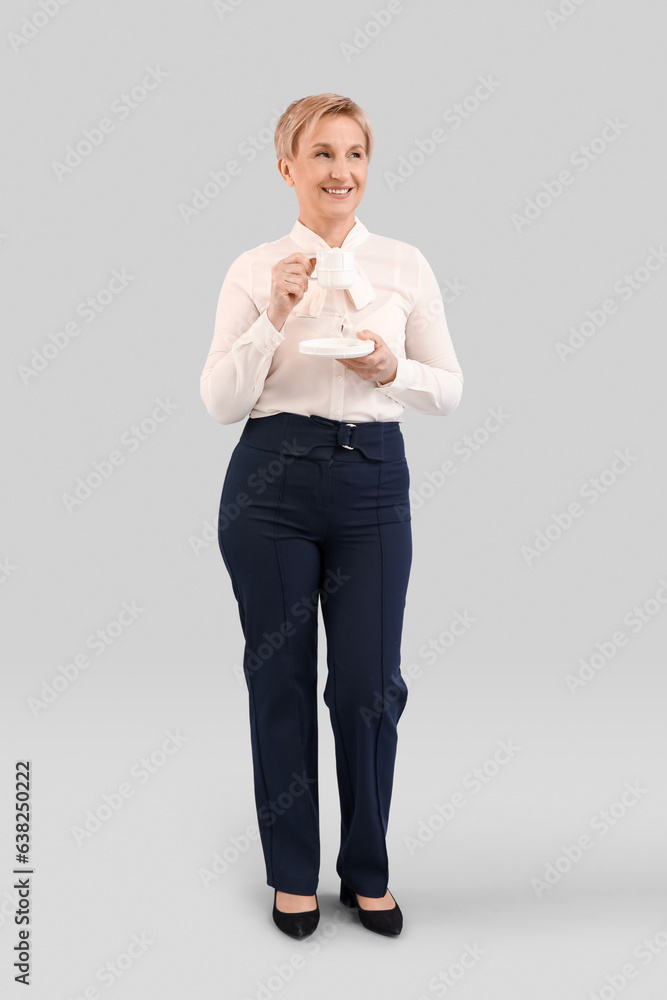 Mature businesswoman drinking coffee on grey background