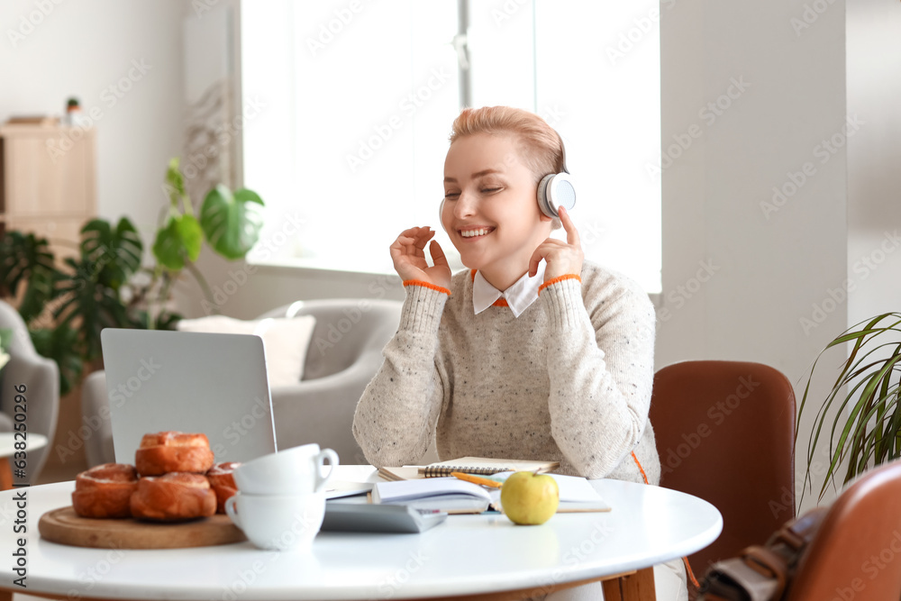 Female student in headphones studying with laptop at home