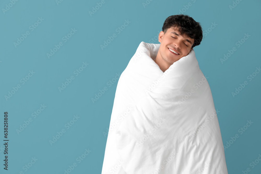 Handsome happy young man wrapped in soft blanket sleeping on blue background