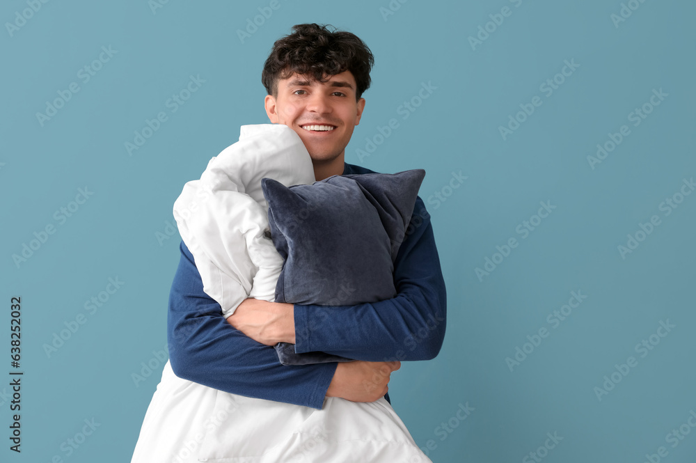 Handsome happy young man with soft blanket and pillow on blue background