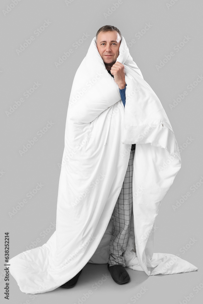 Mature man with soft blanket on grey background