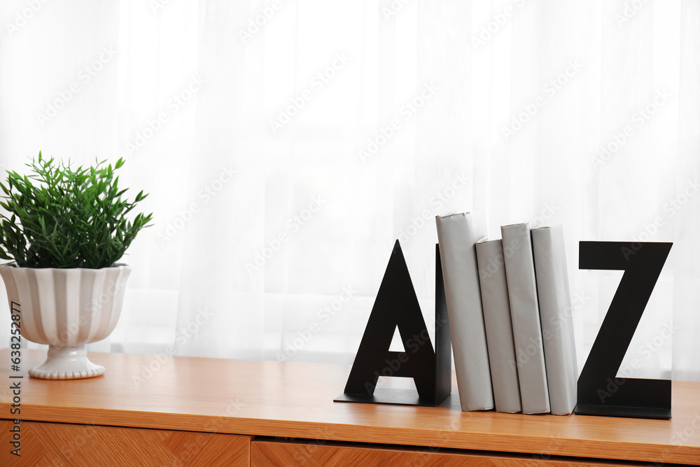 Stylish holder for books with houseplant on wooden commode