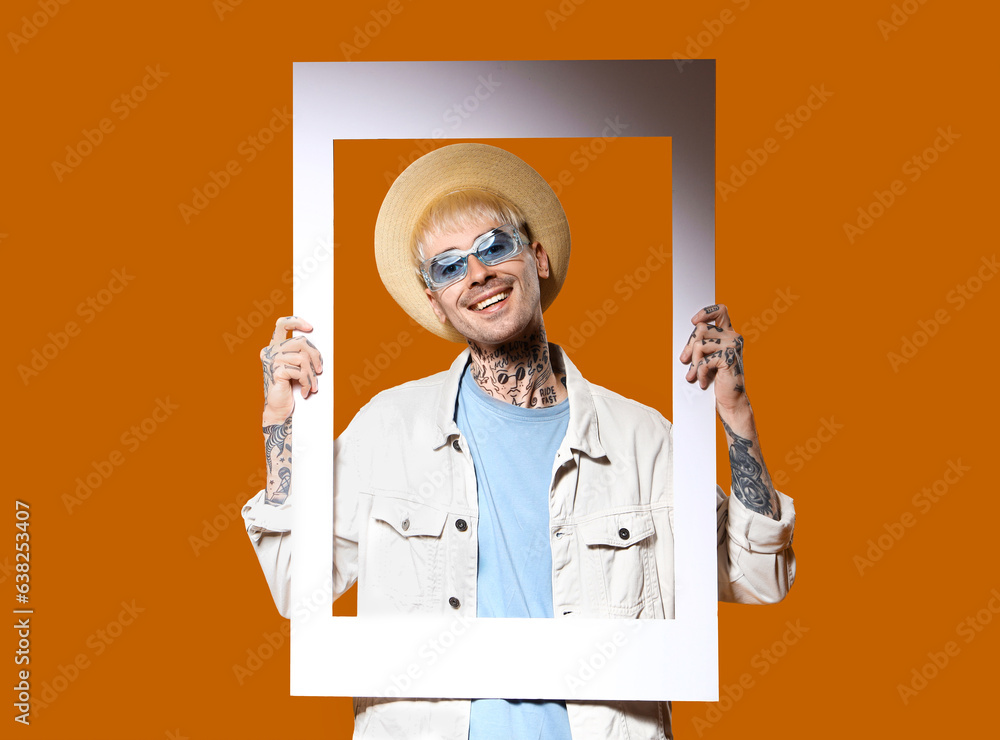 Young tattooed man in stylish sunglasses with frame on color background